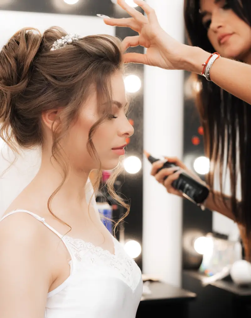 Hair stylist φτιάχνει το νυφικό χτένισμα, η νύφη με πέπλο μπροστά στον καθρέφτη