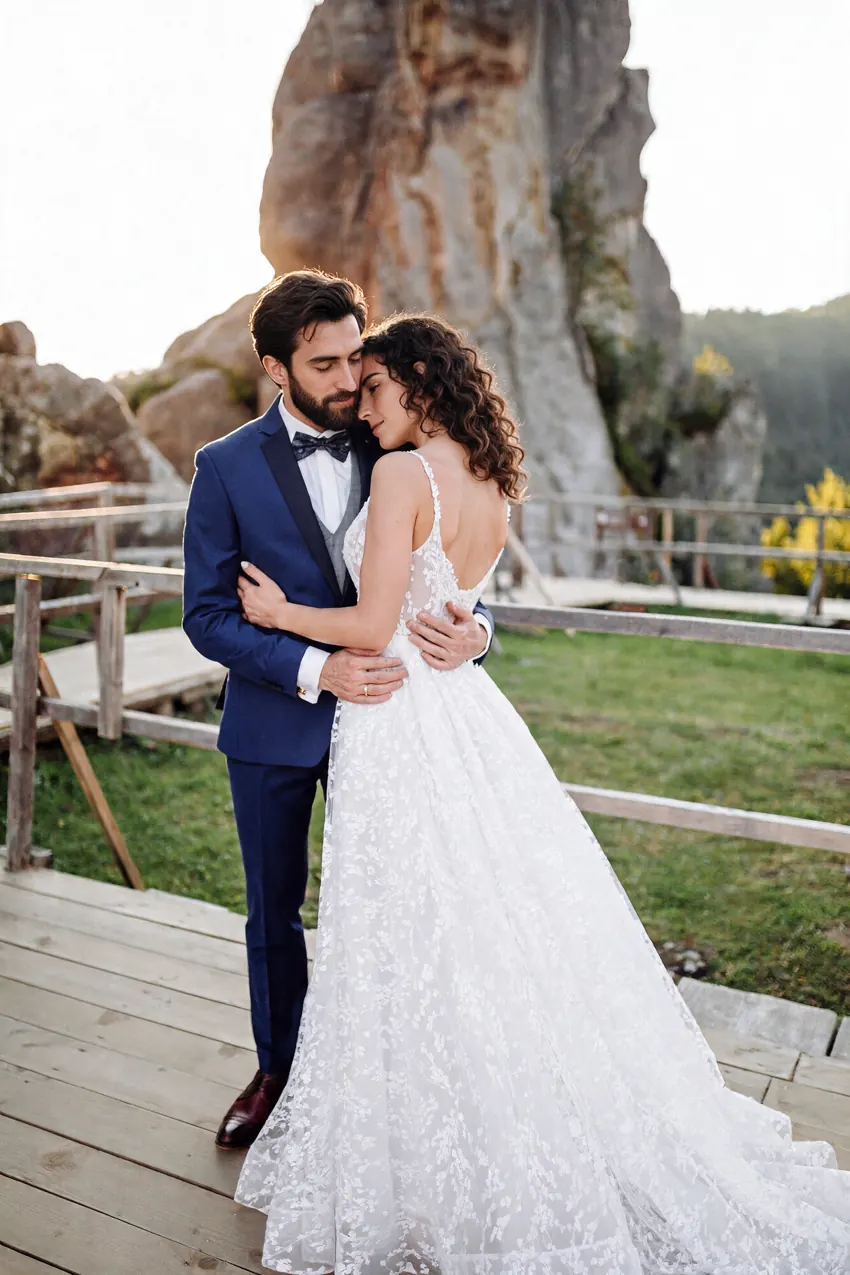 Bride and groom embracing on a wooden deck in front of rocks and green hills