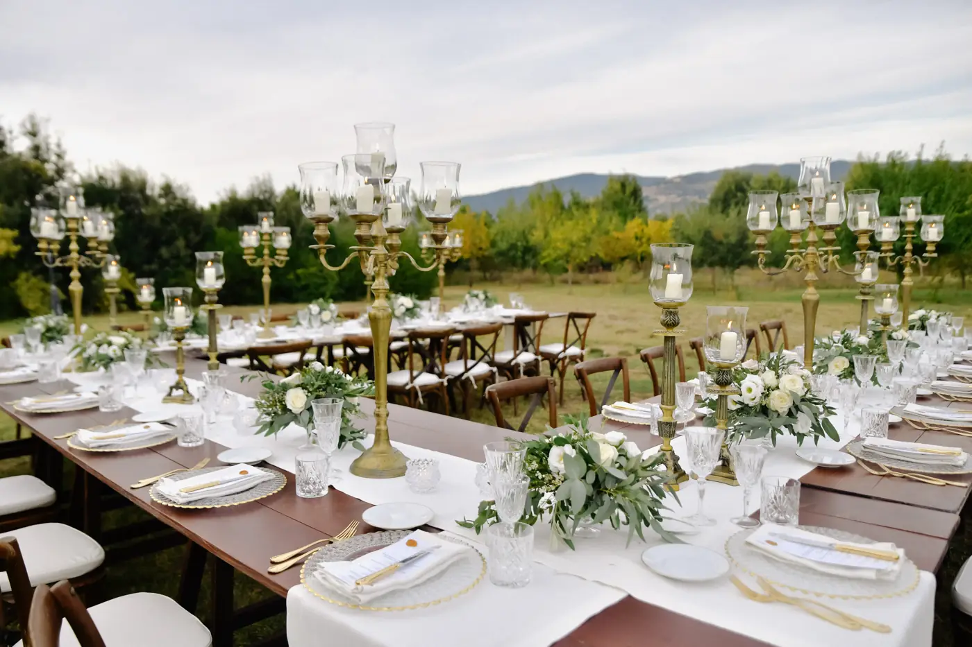 Wedding tables laid in a garden with gold candelabras, white flowers and mountains behind